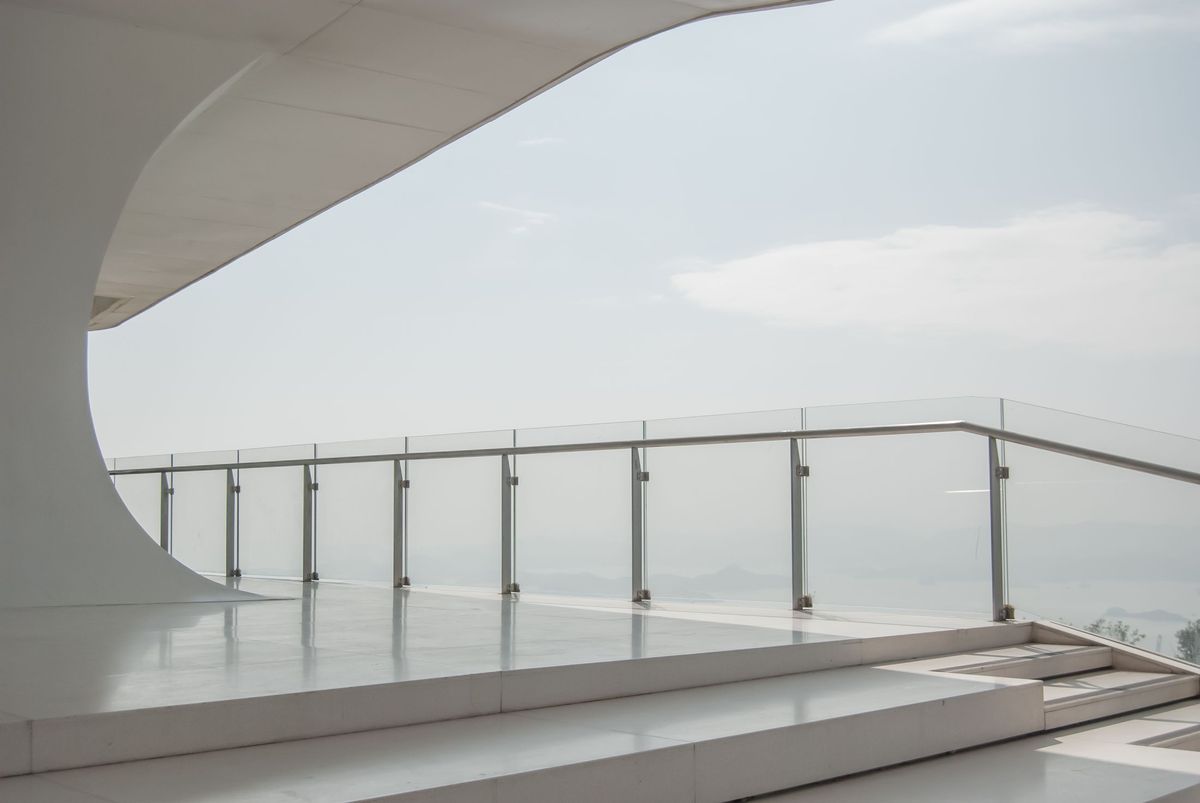 Curved glass balustrade with stainless posts and a handrail on a terrace overlooking the sea