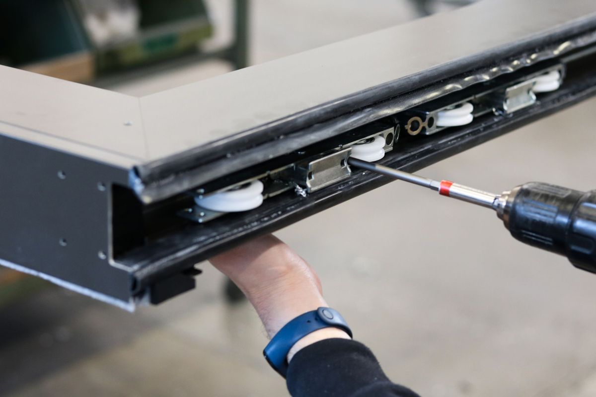 Hands fitting rollers into a black aluminium sliding sash profile with a drill