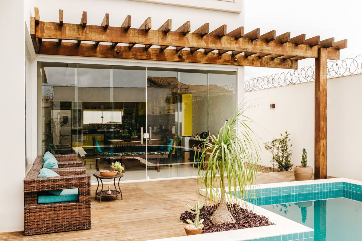 Frameless glass folding panels under a timber pergola beside a pool
