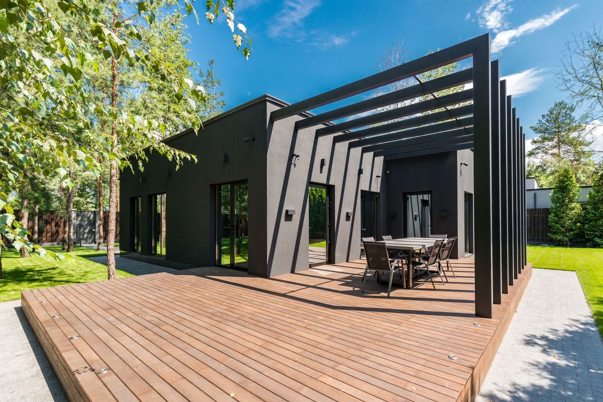 Black pergola frame over a timber deck beside a dark modern house