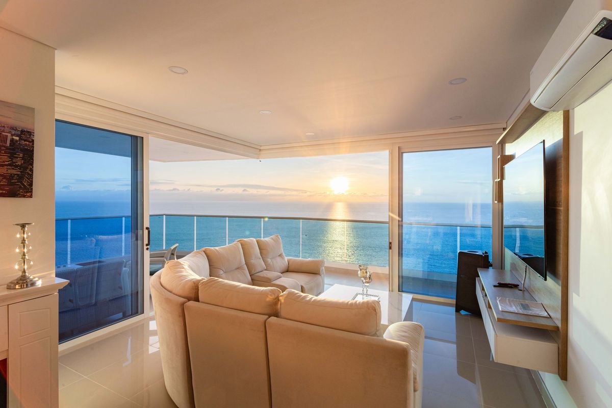 Full-height sliding doors opening a living room onto a sea-facing balcony at sunset