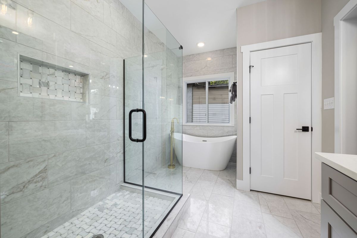 Frameless hinged glass shower door with a black handle and marble walls