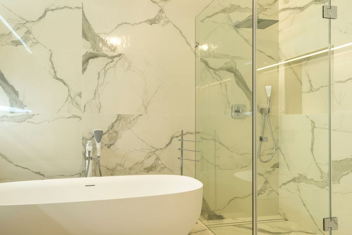 Frameless glass shower screen beside a freestanding bath with marble walls