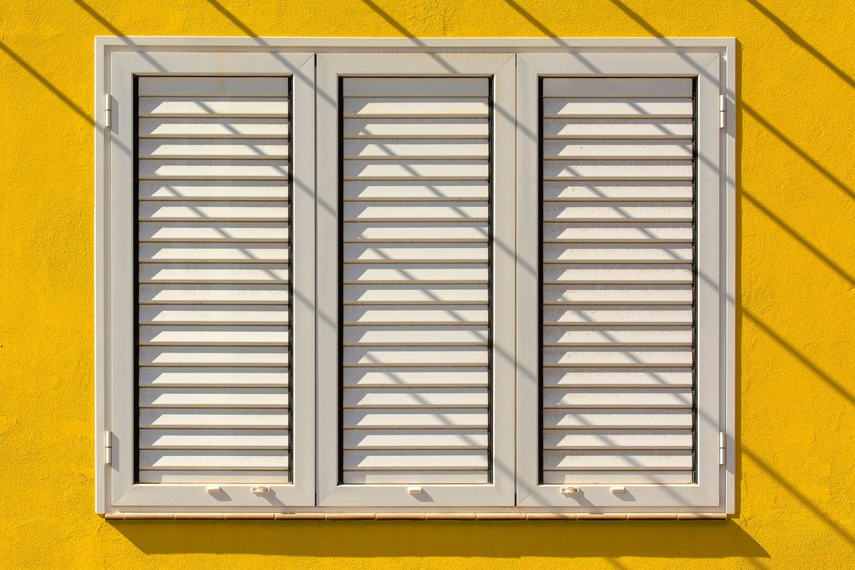 Three louvre shutter panels on a yellow wall